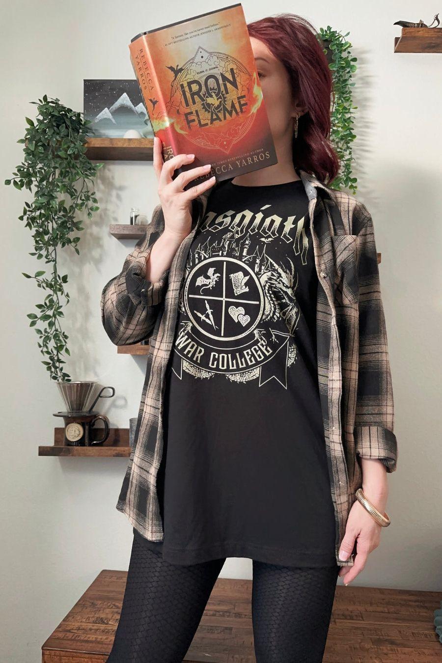 Woman wearing a black T-shirt featuring a Basgiath War College crest with fantasy symbols, dragons. Officially Licensed Fourth Wing Merch.