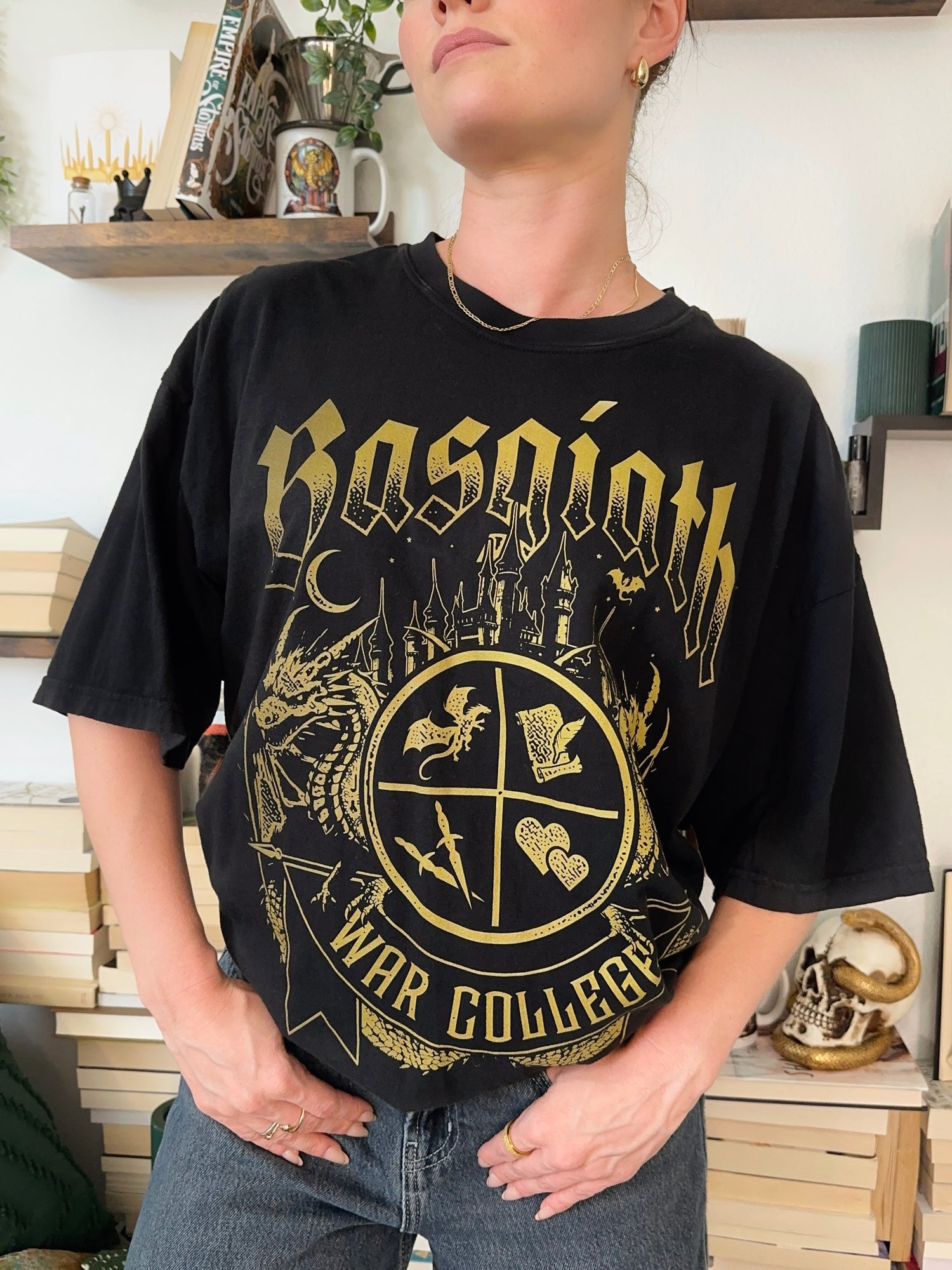 Woman wearing a black T-shirt featuring a Basgiath War College crest with fantasy symbols, dragons. Officially Licensed Fourth Wing Merch.
