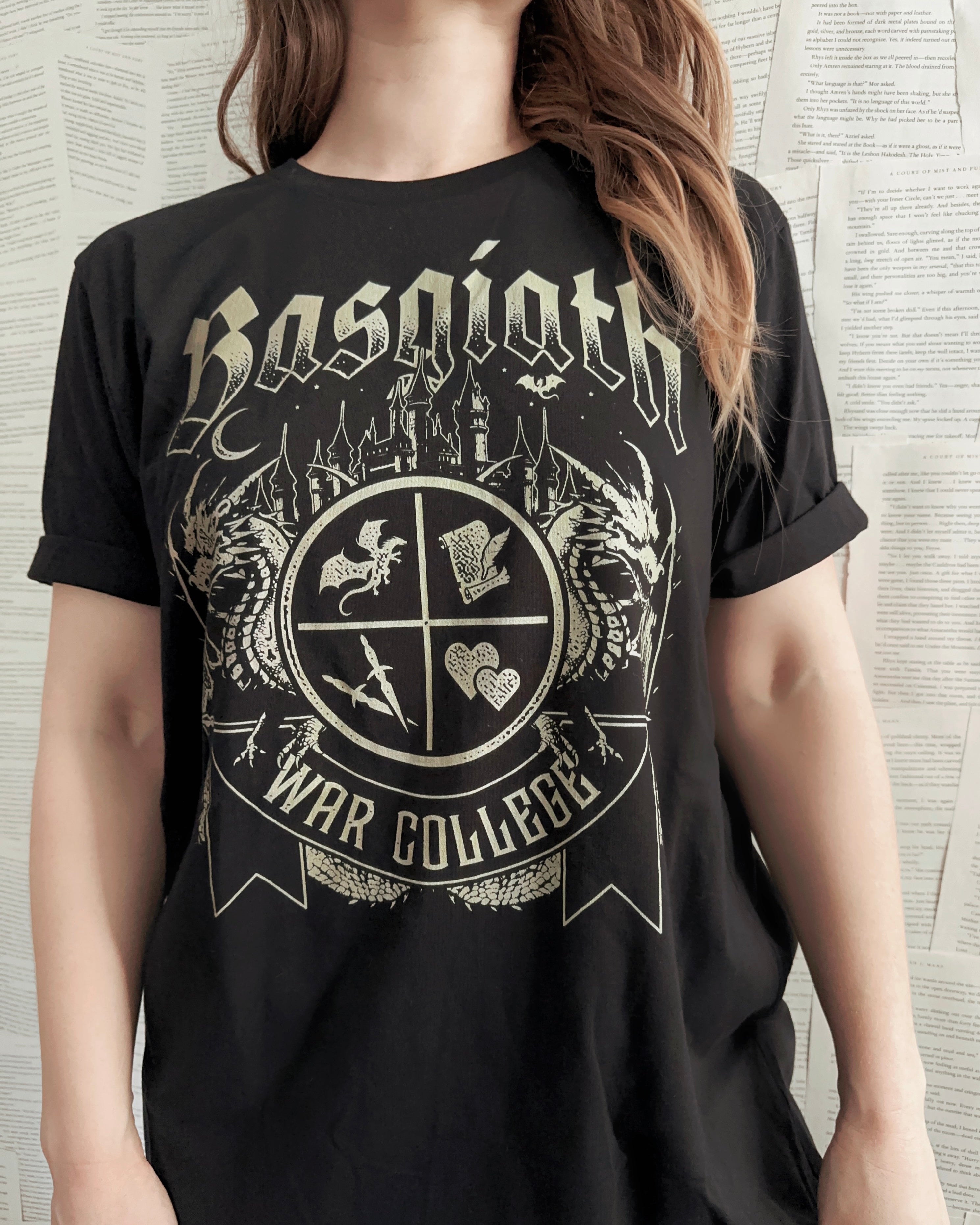 Woman wearing a black T-shirt featuring a Basgiath War College crest with fantasy symbols, dragons, and gothic lettering, inspired by Fourth Wing.