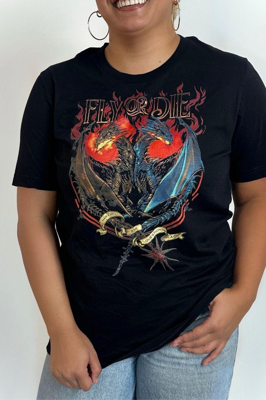 Woman wearing Fly or Die Fourth Wing black T-shirt with twin dragons with flame background, styled with light blue jeans on a white background.