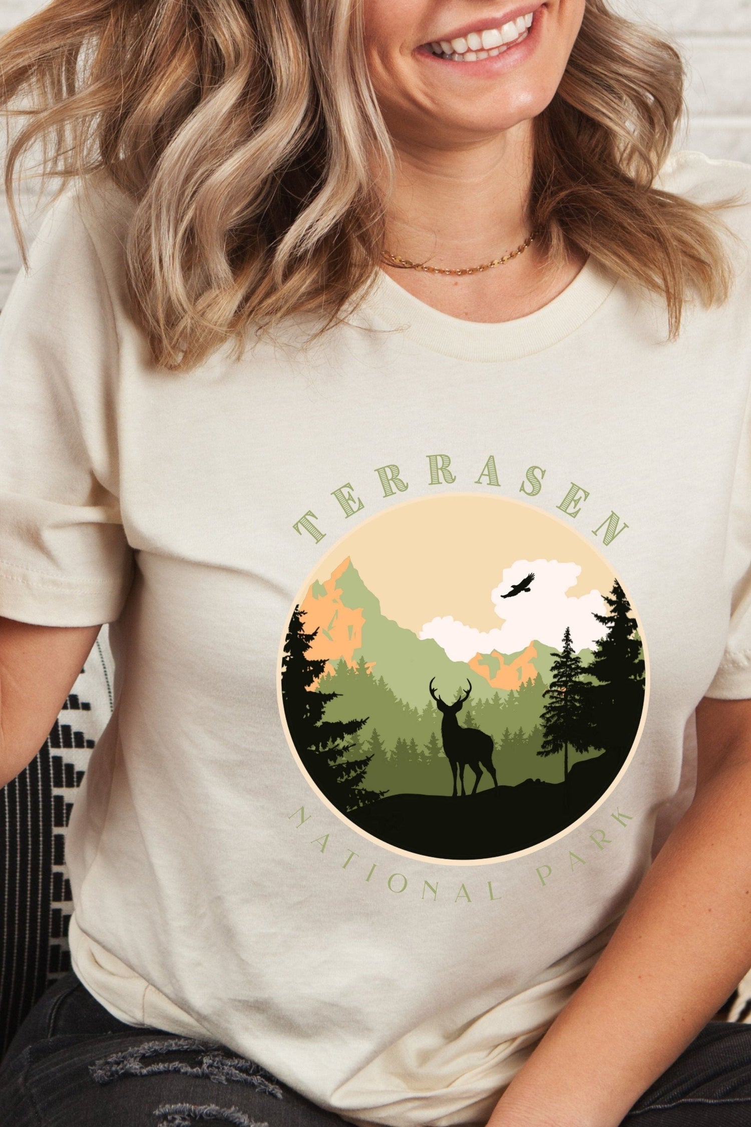 Cream Terrasen t-shirt with circular National Park-style graphic showing a stag in a pine forest with mountains, inspired by Throne of Glass by Sarah J Maas
