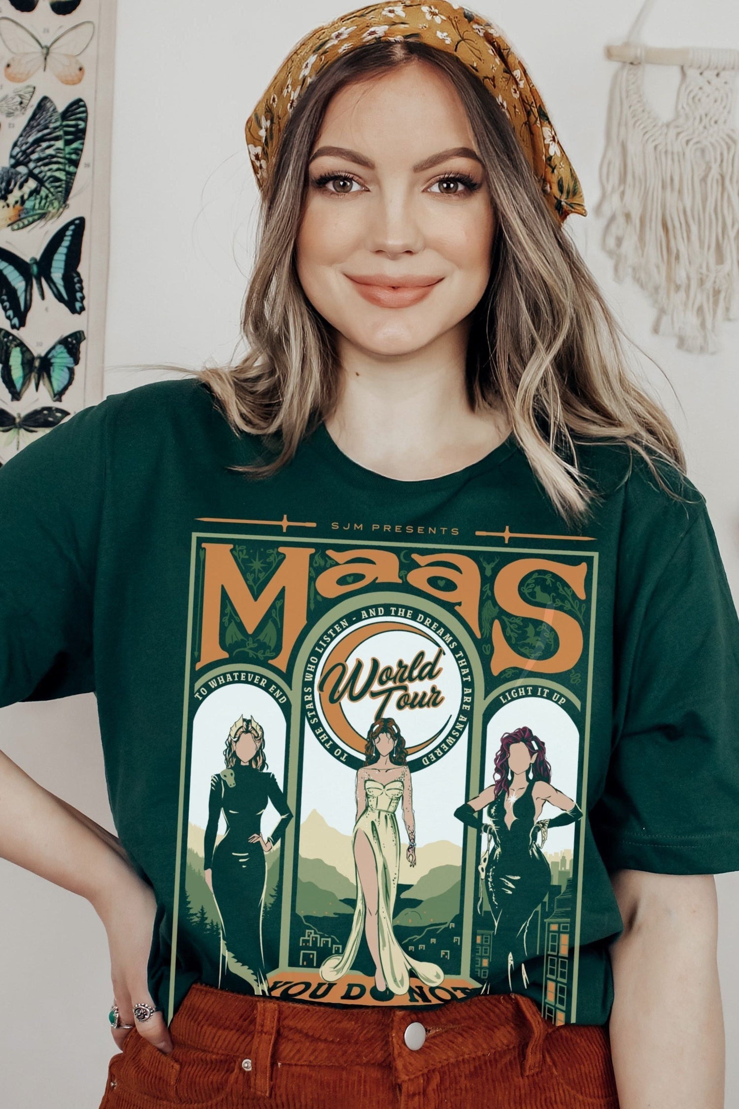 Model wearing a green t-shirt from the Maasverse collection, featuring a vintage-style “Maas World Tour” design with Bryce Quinlan (Crescent City), Feyre Archeron (ACOTAR), and Aelin Galathynius (Throne of Glass)—from the books by Sarah J. Maas