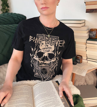 Person wearing a black t-shirt with a skull design, sitting on a couch with books around.