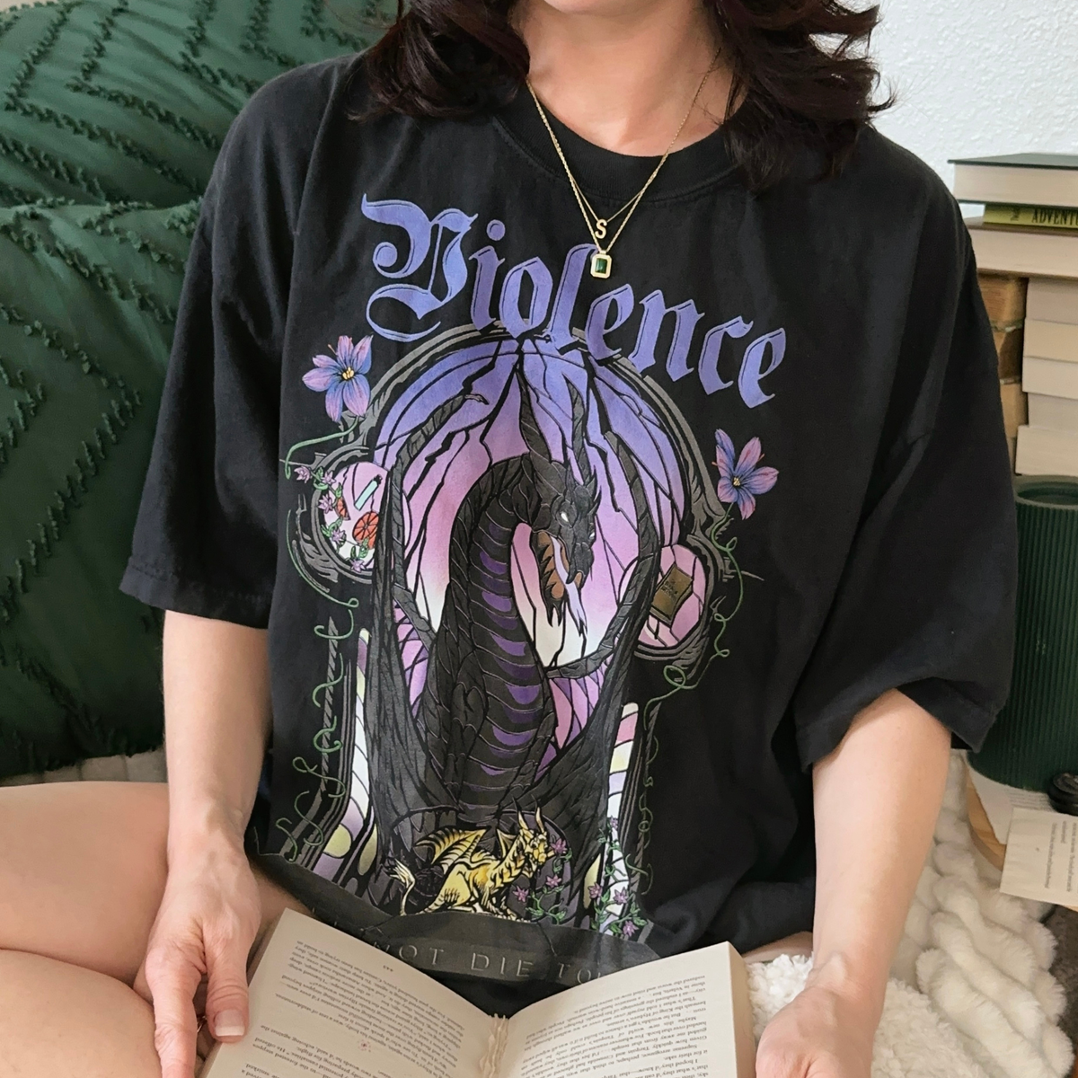 Model wearing the black Violence t-shirt — the stained-glass arch in purple and lilac with the dark winged dragon and the golden hatchling at its base