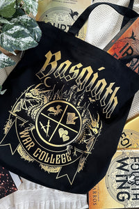 Black Basgiath War College tote bag with gold dragon crest design, surrounded by Fourth Wing books in cozy flatlay.
