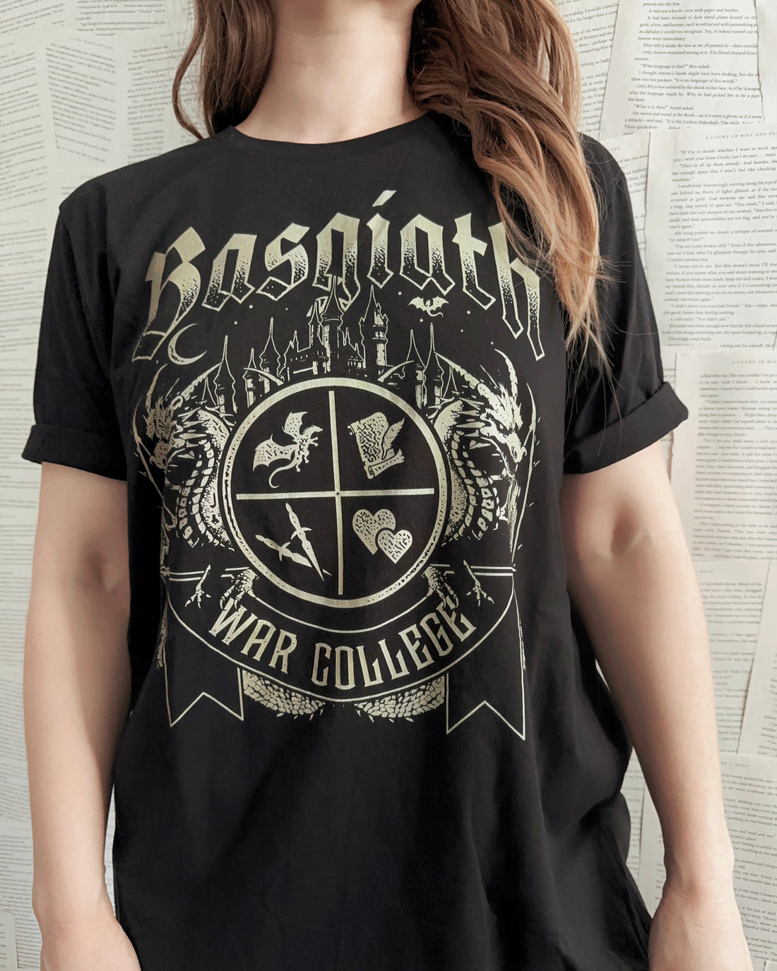 Woman wearing a black T-shirt featuring a Basgiath War College crest with fantasy symbols, dragons, and gothic lettering, inspired by Fourth Wing.