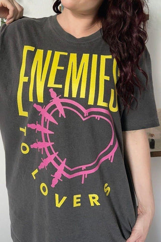 Women wearing a black t-shirt with bold yellow text reading “Enemies to Lovers” and a distressed pink barbed-wire heart graphic - designed for romance readers 