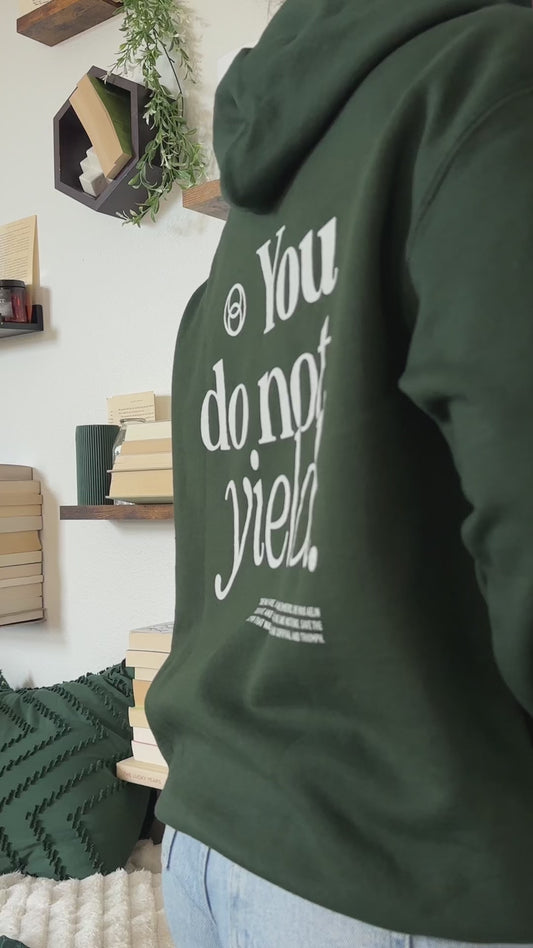 Try-on video: forest green You Do Not Yield hoodie, the cream serif back print reading 'You do not yield.' beneath a circular mark, with the smaller quote block below, and the matching chest print [focal 50 30]
