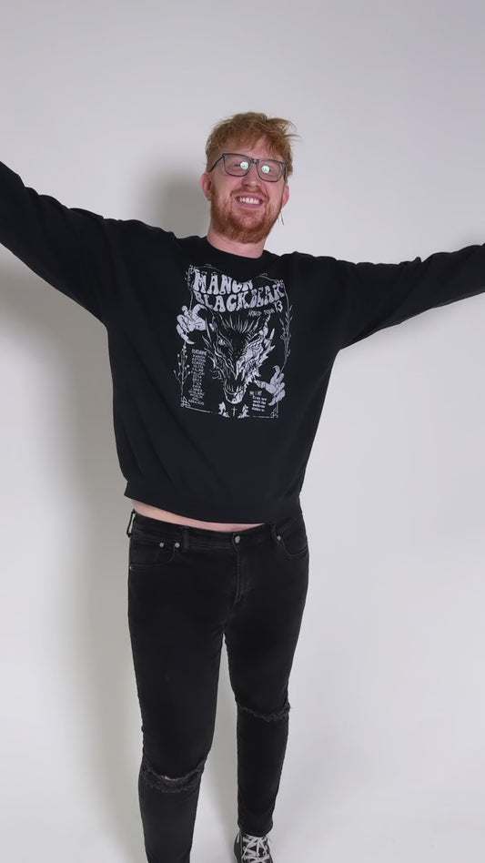 Fit video: four different models wearing the black Manon Blackbeak sweatshirt against a studio backdrop — the white tour-poster print with 'The Thirteen presents', MANON BLACKBEAK, World Tour 13 and the wyvern [focal 50 30]