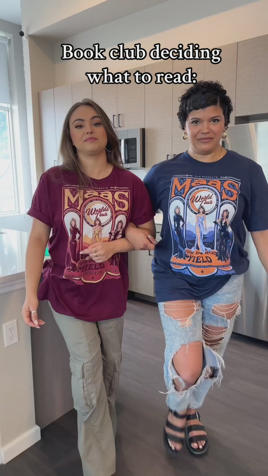 Try-on video: the maroon Maasverse t-shirt worn alongside the navy — the art-nouveau tour-poster print with MAAS, the World Tour roundel, the three figures and 'you do not yield' [focal 50 40]