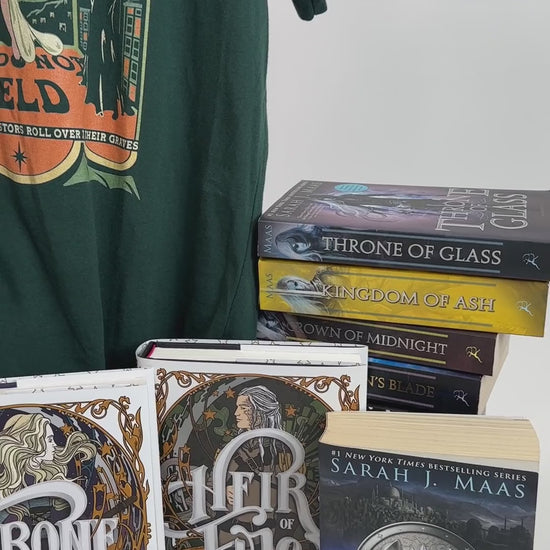 Product video: the forest green Maasverse t-shirt on the hanger with the Throne of Glass hardbacks — the art-nouveau tour poster with 'SJM Presents', MAAS, the World Tour roundel, the three figures in their arches and 'you do not yield' beneath [focal 50 30]