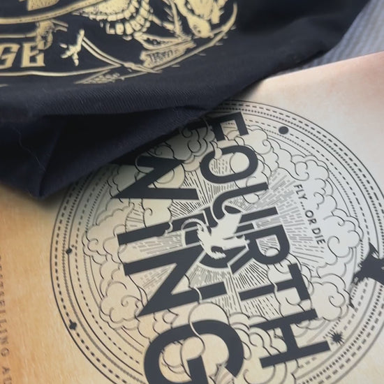 Product video: the black Basgiath War College tote with the Fourth Wing and Iron Flame hardbacks — the gold gothic Basgiath lettering above the War College crest and banner [focal 50 50]