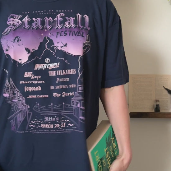 Try-on video: the navy Starfall Festival t-shirt worn with a book — the lilac and peach night sky over the mountain, the Inner Circle line-up beneath and Rita's along the hem [focal 50 25]