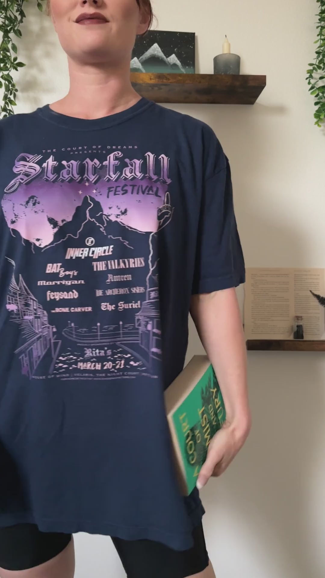 Try-on video: the navy Starfall Festival t-shirt worn with a book — the lilac and peach night sky over the mountain, the Inner Circle line-up beneath and Rita's along the hem [focal 50 25]