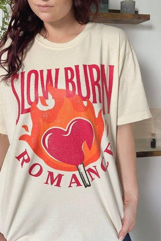 Female wearing a Cream-colored t-shirt with a flaming heart and match design, featuring bold red text that reads “Slow Burn Romance” - a cozy, trope-inspired piece of book merch.