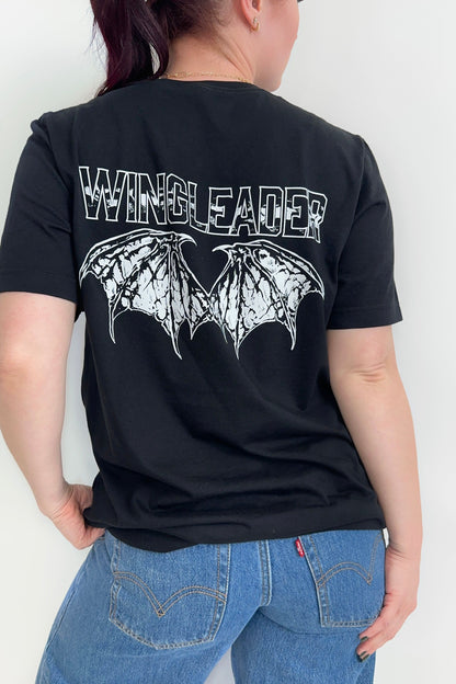 Back view of a black unisex t-shirt with “Wingleader” text and white wingspan illustration in distressed print, worn with jeans