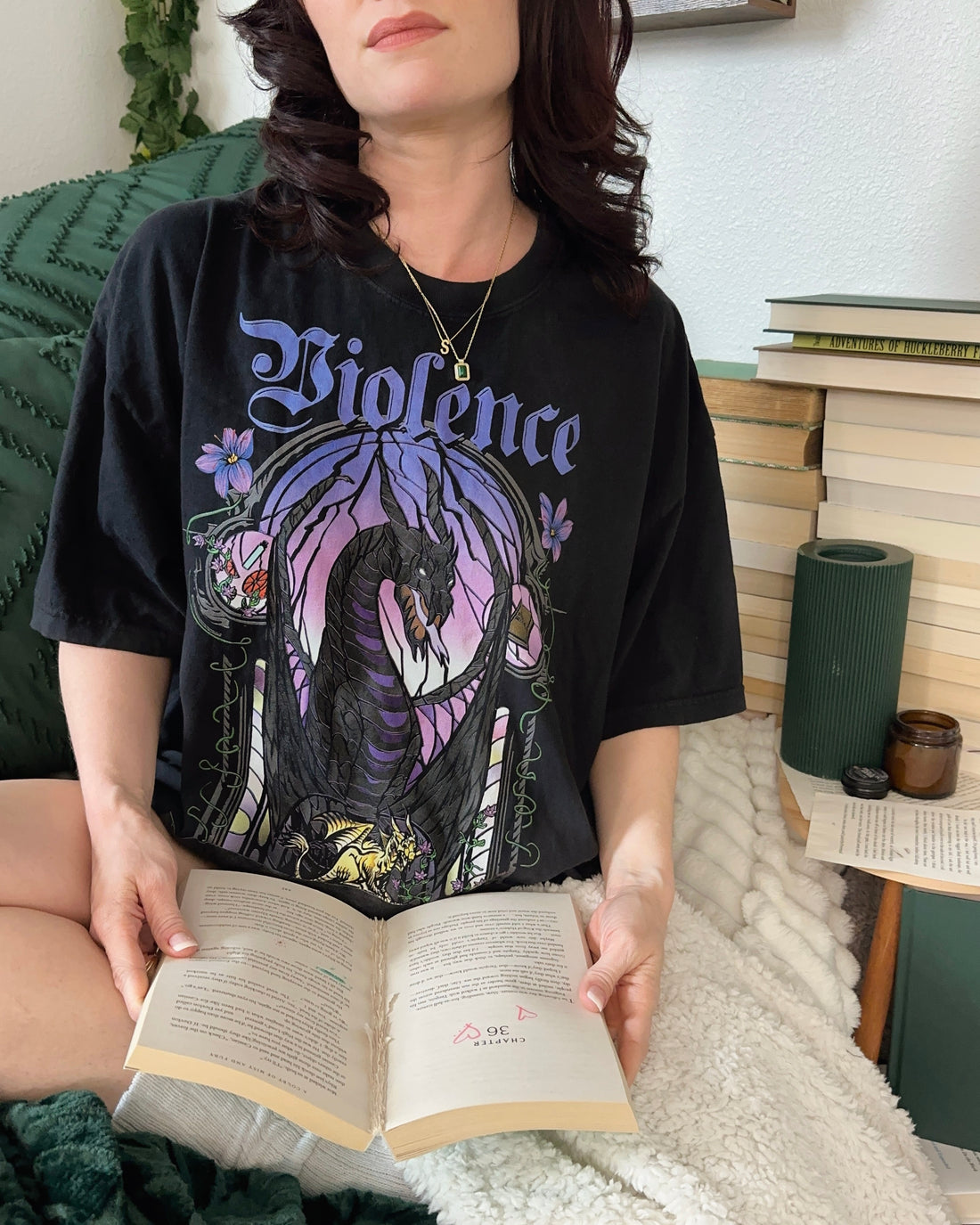 Woman wearing Violence Fourth Wing tee, inspired by Violet, Tairn, and Andarna, while reading on a cozy blanket.